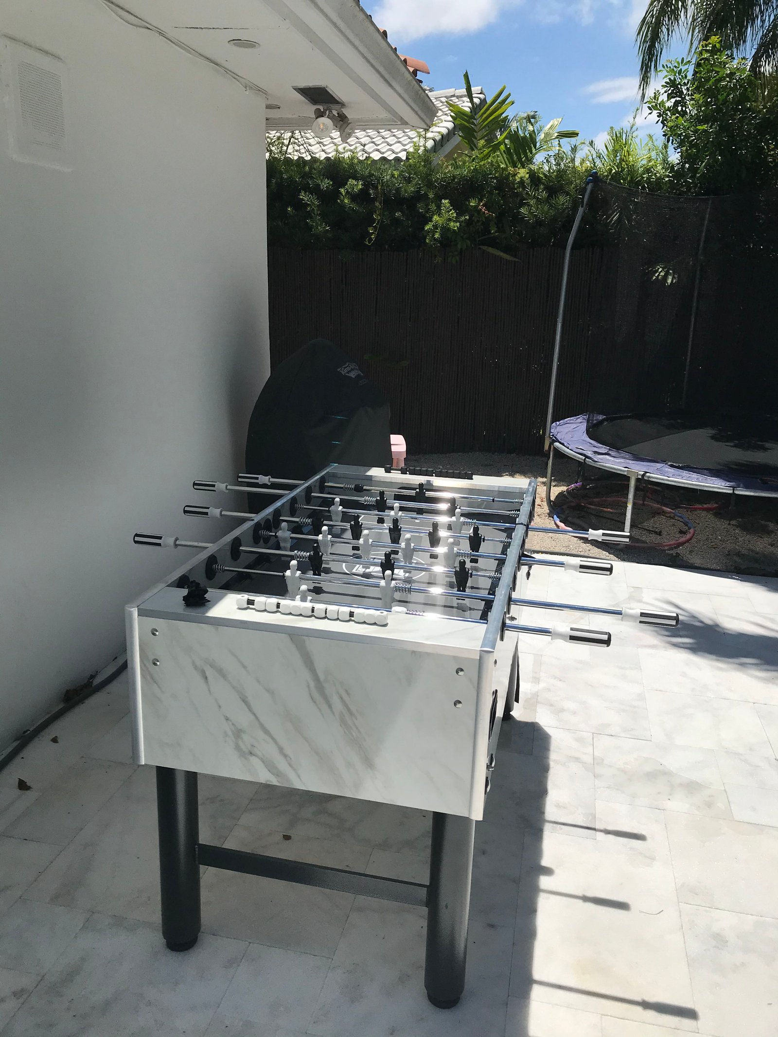 A Kettler Carrara outdoor foosball table stands by the trampoline and grill.