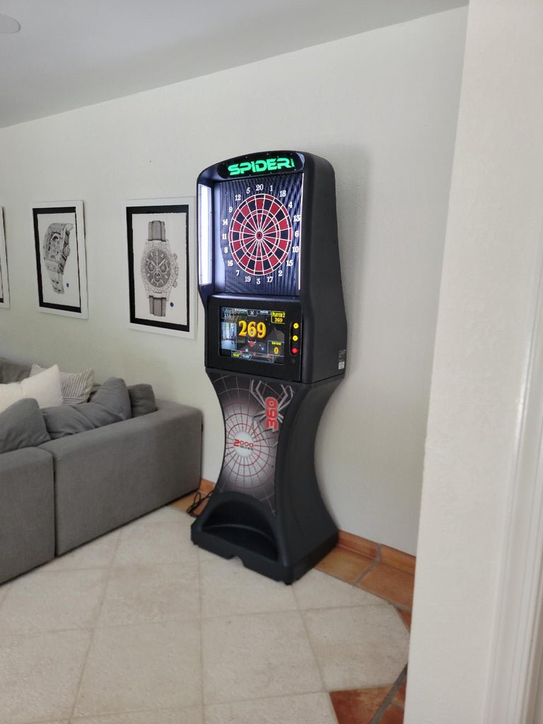 An Arachnid Spider 360 2000 Series electronic dartboard sits near a gray couch.