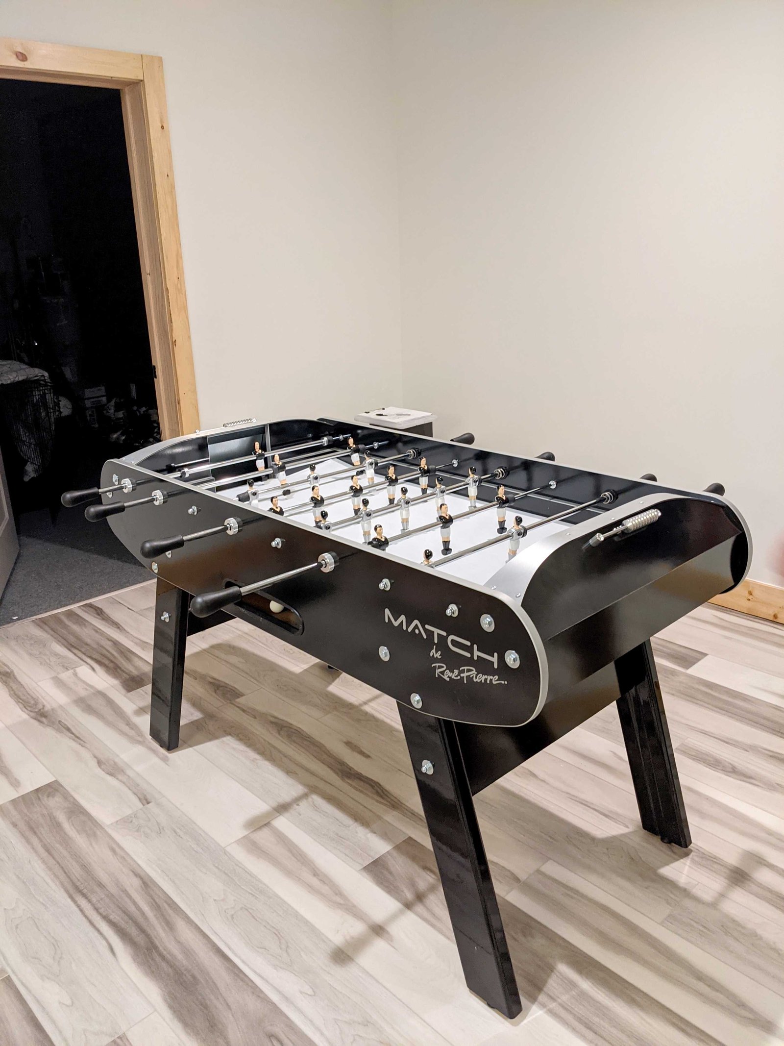 Rene Pierre Match Foosball Table in Black in a game room with light wood floors and cream walls.