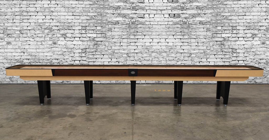 Venture Classic Coin 16' Shuffleboard Table with black legs, white brick wall, concrete floor.