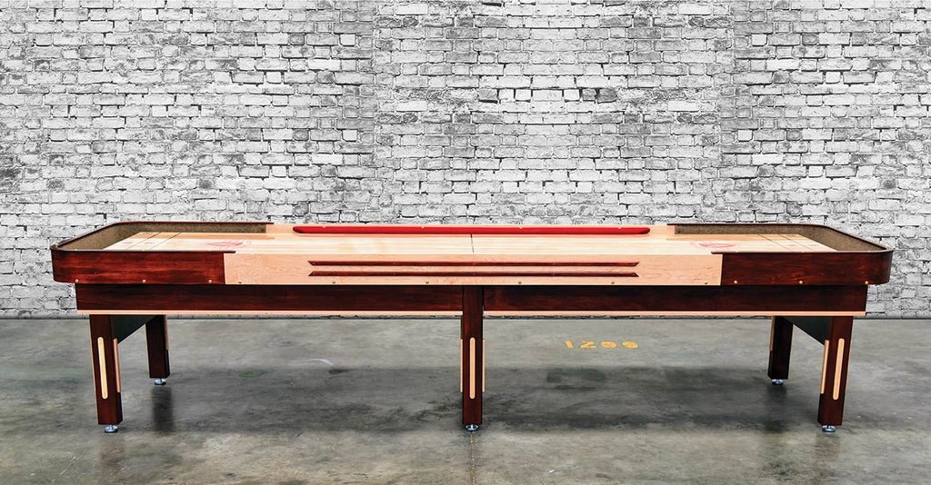 A Venture Grand Deluxe Cushion 12' Shuffleboard Table stands on a concrete floor by a brick wall.