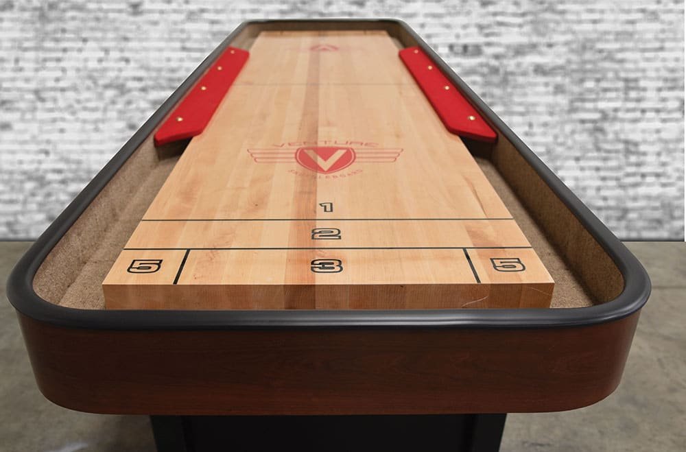 Venture Classic Bank Shot 9' Shuffleboard Table with red bumpers and white brick wall background.